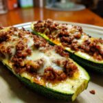 Two baked Ground Beef Zucchini Boats topped with melted cheese on a plate.