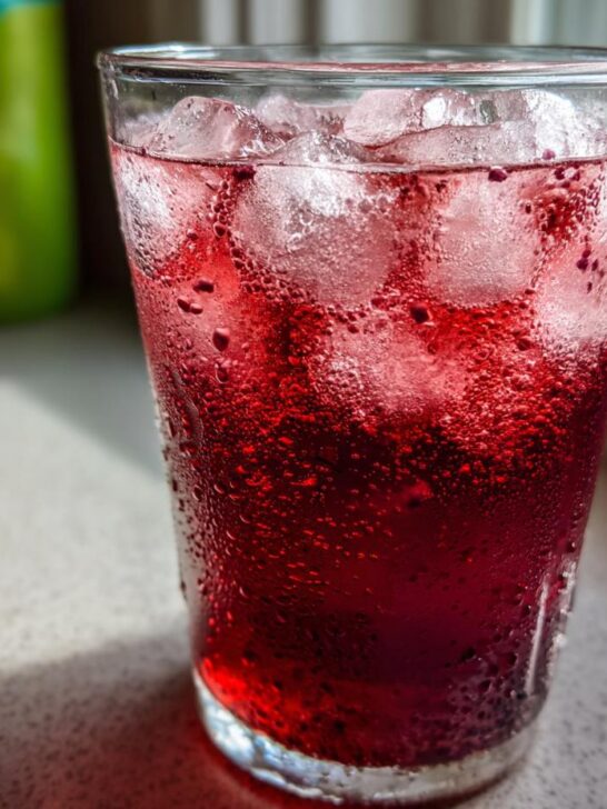 Close-up of a tall glass filled with an icy, deep red, carbonated Healthy Blood Orange Kiwi Drink.