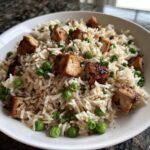 Close-up of a bowl containing a High Protein One Pot Dinner featuring rice, green peas, and seared tofu cubes.