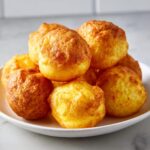 A close-up of several golden brown Homemade Corn Dog Bites piled high on a white serving plate.