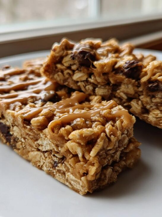 Three chewy Homemade No Bake Granola Bars stacked on a white plate, drizzled with caramel or peanut butter.