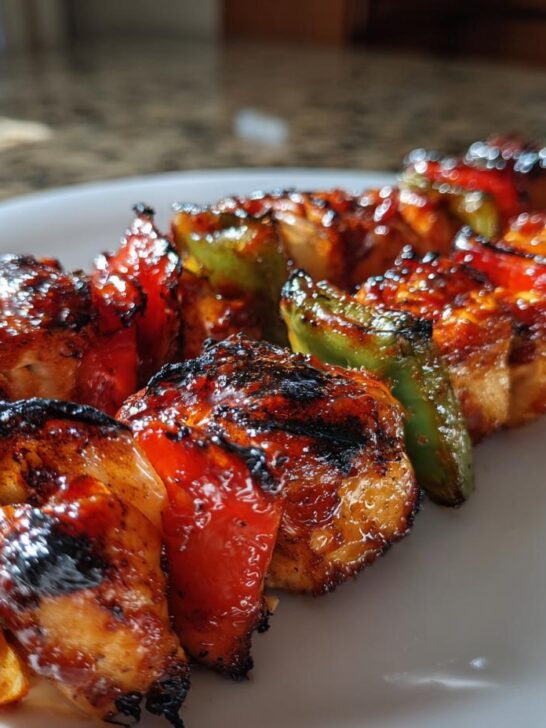 Close-up of grilled Honey Bbq Chicken Kabobs featuring charred chicken pieces and vibrant red and green bell peppers.