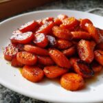 A close-up of beautifully caramelized Honey Roasted Carrots, glistening with glaze on a white plate.