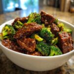 A close-up shot of glossy, saucy Instant Pot Beef And Broccoli served in a white bowl.