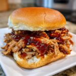 Close-up of a delicious Instant Pot Pulled Pork Sandwich piled high with saucy meat on a soft bun.