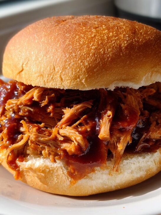 A close-up of a juicy Instant Pot Pulled Pork Sandwiches piled high on a soft bun with barbecue sauce.