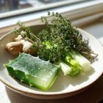 A bowl containing aloe vera, ginger root, thyme sprigs, and scallions, representing Jamaican Herbs That You Should Always Keep On Hand Remedies.