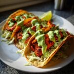Three Jerk Salmon Tacos topped with shredded cabbage and a generous drizzle of Avocado Cilantro Lime Sauce.