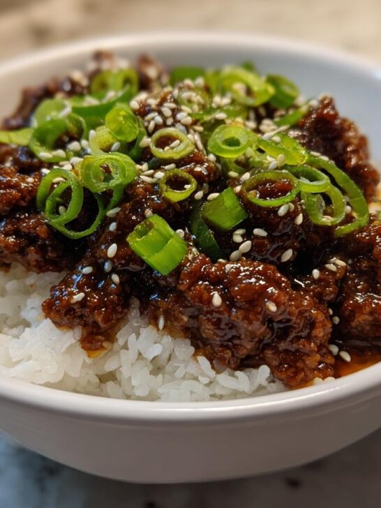 A close-up of a Korean Ground Beef Bowl featuring saucy ground beef over white rice, topped with green onions and sesame seeds.