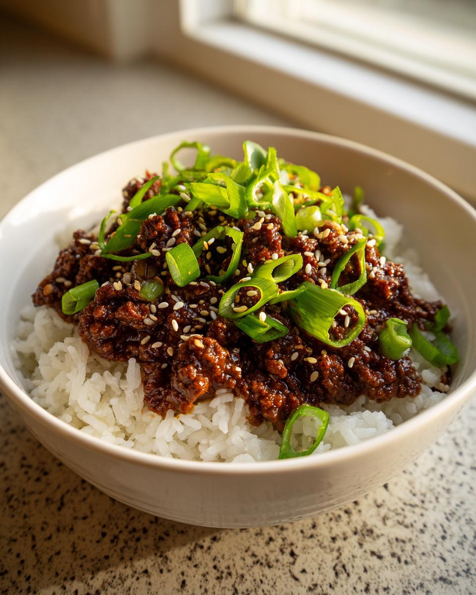 A close-up of a Korean Ground Beef Bowl served over white rice, topped with sesame seeds and fresh green onions.