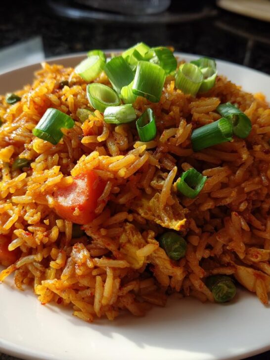 A plate of vibrant, orange-hued Korean Veggie Fried Rice mixed with peas and carrots, topped with fresh green onions.