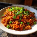 A close-up of vibrant Korean Veggie Fried Rice mixed with peas and carrots, topped generously with fresh green onions.