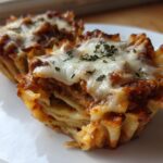Two baked Lasagna Cups showing layers of pasta, rich meat sauce, and melted mozzarella cheese topped with herbs.