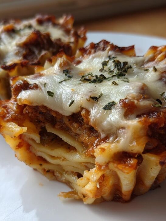Two baked Lasagna Cups showing layers of pasta, rich meat sauce, and melted mozzarella cheese topped with herbs.