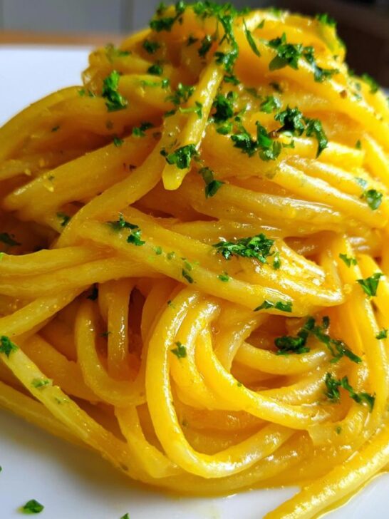 Close-up of a serving of bright yellow Lemon Butter Linguine pasta, glistening and topped with fresh chopped parsley.