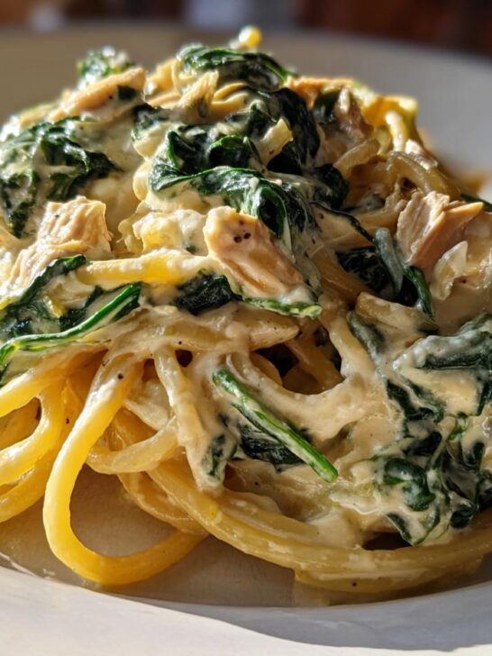 Close-up of creamy Lemon Ricotta Pasta With Spinach tossed with spaghetti and wilted greens on a white plate.