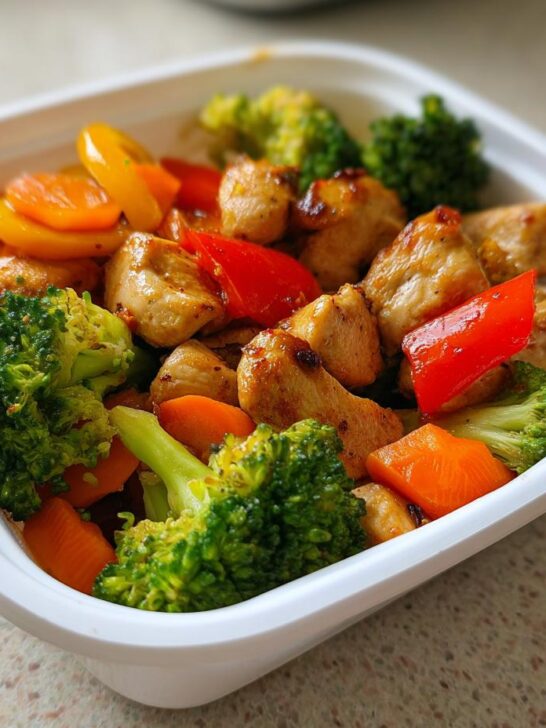 Close-up of a single serving meal prep container filled with seasoned chicken chunks, broccoli, carrots, and bell peppers.