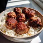Close-up of a bowl filled with white rice topped with seven perfectly browned Meatballs And Rice Bowl components.