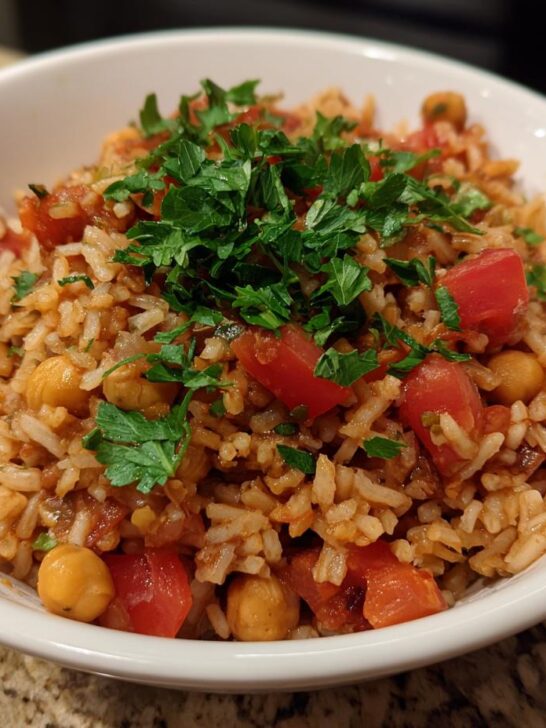 A white bowl filled with Mediterranean Rice And Beans, featuring rice, chickpeas, diced tomatoes, and topped with fresh parsley.