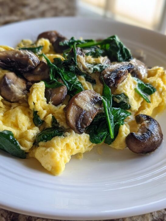 Fluffy yellow Mushroom Spinach Scrambled Eggs served on a white plate, ready to eat.