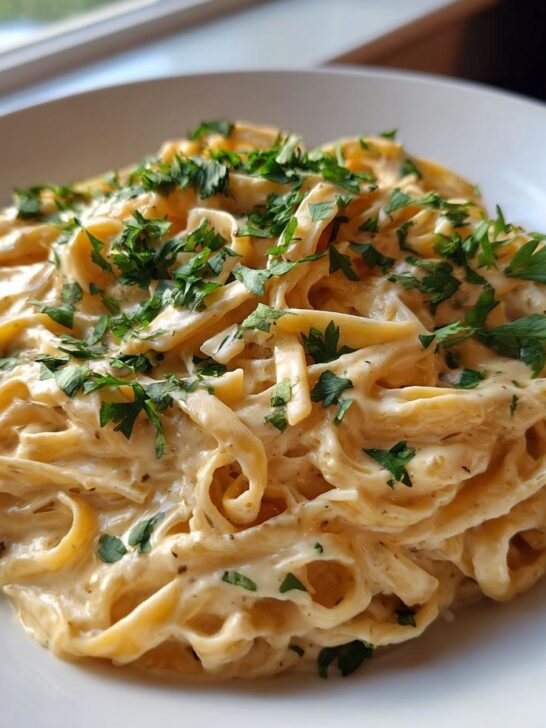 A close-up of rich, creamy fettuccine pasta topped with fresh chopped parsley, representing One Pot Creamy Garlic Pasta.