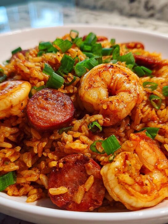 A close-up of a white bowl filled with flavorful 1 Pot Shrimp And Sausage Jambalaya, topped with green onions.