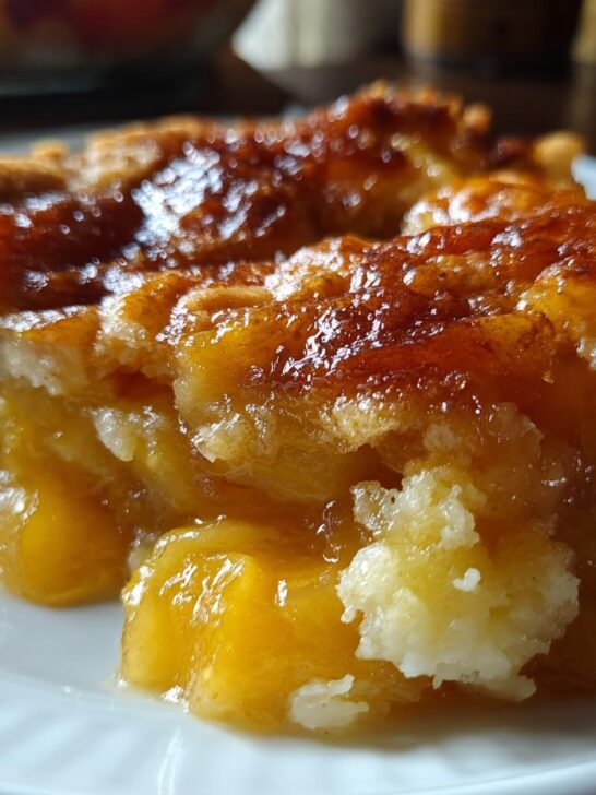 A close-up of a warm, gooey serving of Peach Cobbler With Canned Peaches on a white plate.