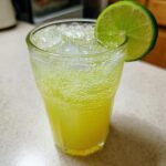 A glass filled with a fizzy, yellow Pineapple Jalapeno Lime Mocktail, garnished with a fresh lime wheel.