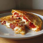 Two halves of a golden-brown Pizza Quesadillas spilling melted cheese and pepperoni slices.