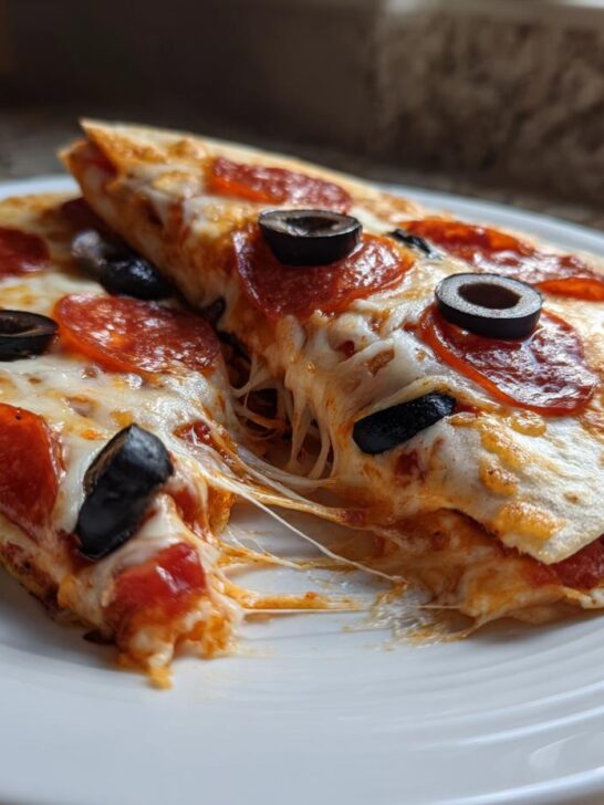 Two slices of Pizza Quesadillas with melted cheese, pepperoni, and black olives, showing a cheese pull.