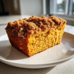 A close-up, sunlit slice of moist Pumpkin Coffee Cake featuring a thick, brown sugar crumb topping.