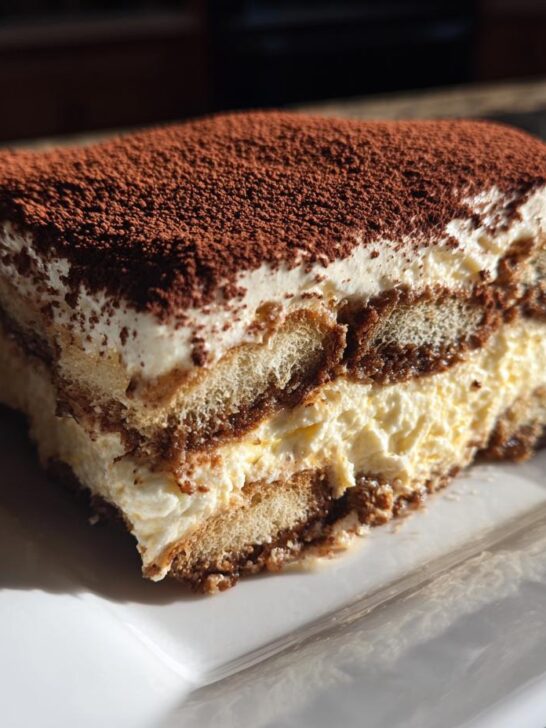 A close-up slice of Pumpkin Spice Tiramisu layered with cream and ladyfingers, topped with cocoa powder.