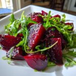 Close-up of a vibrant Roasted Beet And Arugula Salad featuring glossy, deep red beet chunks mixed with fresh green arugula.