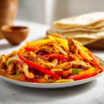 A close-up of seasoned chicken strips mixed with colorful bell peppers and onions, ready for Sheet Pan Chicken Fajitas.