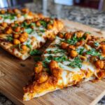 Close-up of a slice of Sheet Pan Roasted Garlic Buffalo Chickpea Pizza topped with melted cheese and fresh cilantro.