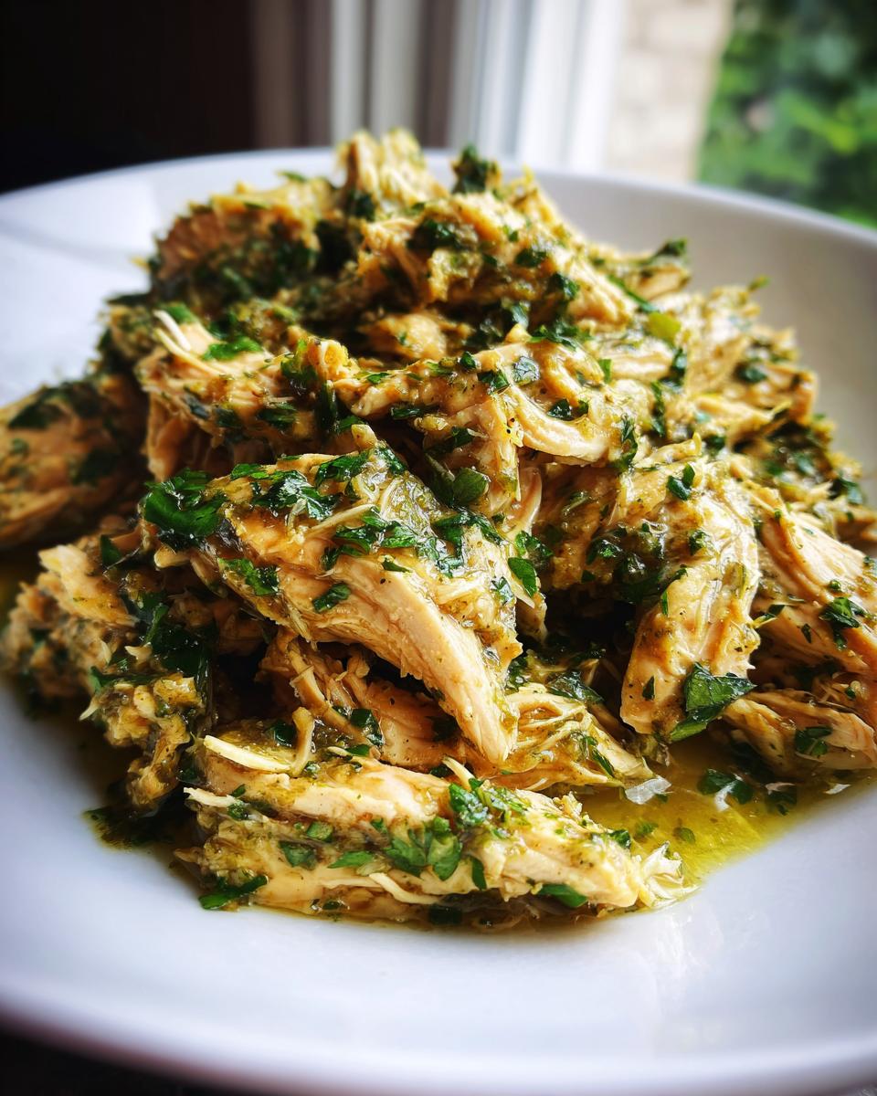 Close-up of tender, shredded Slow Cooker Salsa Verde Chicken topped with fresh green herbs.
