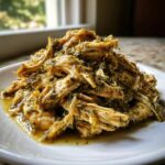 Close-up of shredded Slow Cooker Salsa Verde Chicken piled high on a white plate, glistening with green sauce.