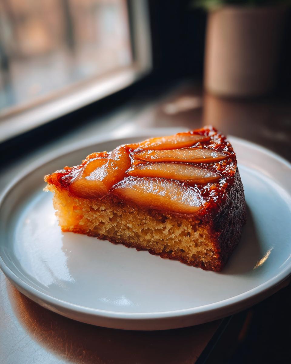 A close-up of a single slice of Spiced Pear Upside Down Cake with caramelized pears on top, served on a white plate.