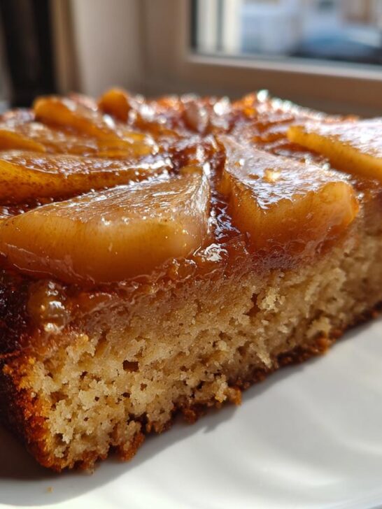 Close-up of a slice of Spiced Pear Upside Down Cake with caramelized pears on top, served on a white plate.