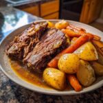 Two slices of shredded, tender Slow Cooker Pot Roast With Vegetables served with roasted potatoes and carrots in gravy.