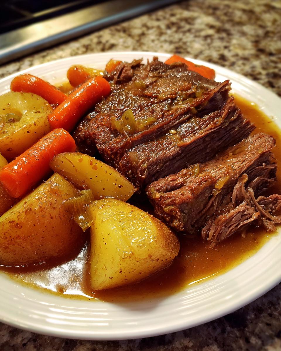 A close-up of sliced Slow Cooker Pot Roast With Vegetables served on a white plate with rich gravy.