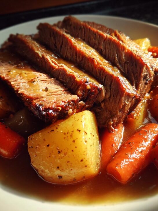 Slices of tender Slow Cooker Pot Roast With Vegetables, including carrots and potatoes, served in rich gravy.