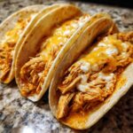Three soft tortillas filled with shredded chicken and melted cheese, ready to eat as Slow Cooker Queso Chicken Tacos.