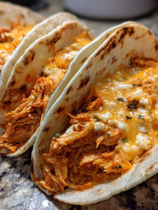 Three soft tortillas filled with shredded chicken and melted queso cheese for Slow Cooker Queso Chicken Tacos.
