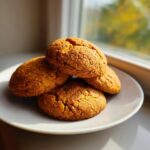 A stack of four soft Chai Spiced Pumpkin Cookies resting on a white plate near a sunlit window.