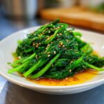 Vibrant green blanched spinach served in a white bowl, drizzled with ponzu sauce and topped with toasted sesame seeds.