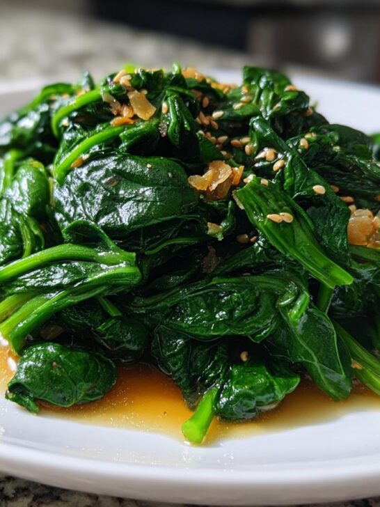Close-up of vibrant green Spinach With Ponzu Sauce Recipe, topped with sesame seeds and garlic.