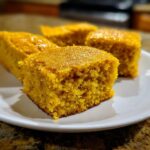 Close-up of four moist, golden squares of Sweet Potato Cornbread served on a white plate.
