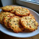 Close-up of several golden brown Sweet Spicy Herb Crackers piled on a white plate.