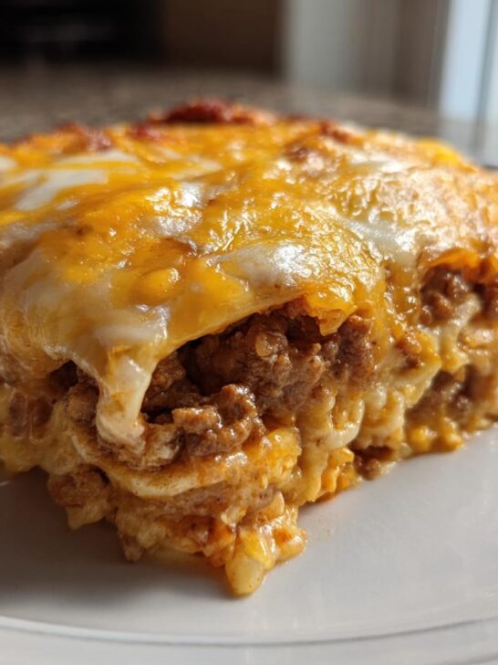 Close-up of a cheesy, layered slice of Taco Bake Casserole topped with melted cheddar and Monterey Jack cheese.